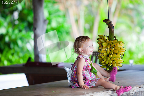 Image of Toddler girl outdoors with bunch of bananas