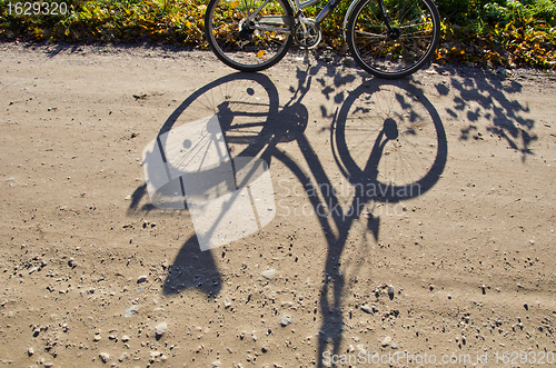 Image of Standing bicycle shadow on gravel road. 