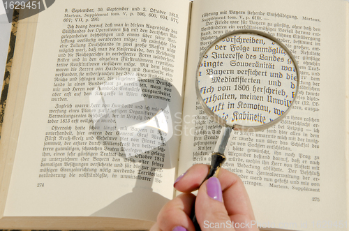 Image of Woman's hand holding magnifying glass over the german book page. 