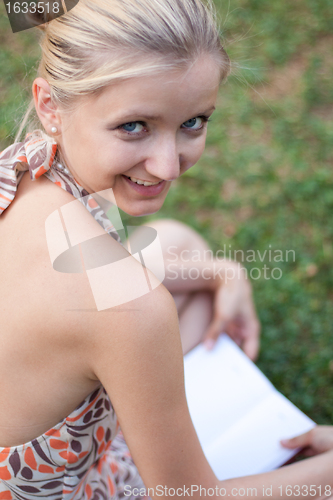 Image of young woman reads the book sits on a green grass