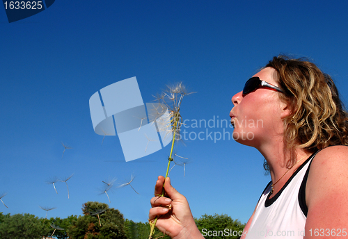 Image of Young woman blowing a dandelion