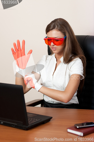 Image of young woman behind table with laptop in gloves