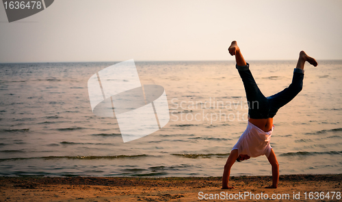 Image of man doing handstand on beach