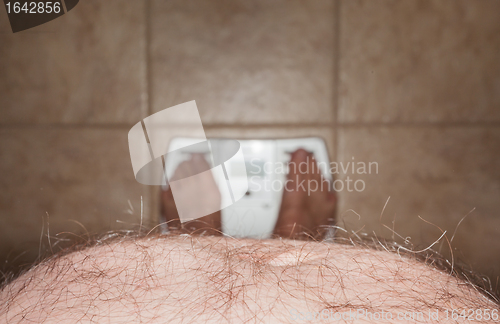 Image of Hairy man stomach overhangs feet on scales