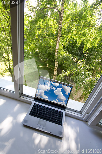 Image of Opened plastic window in room with view to green trees and portable computer