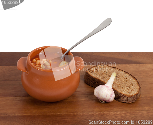 Image of Soup in clay pot with bread and garlic on wooden table