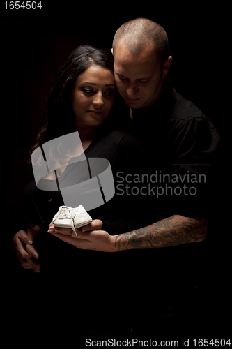 Image of Mixed Race Couple Holding New White Baby Shoes on Black