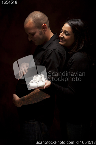 Image of Mixed Race Couple Holding New White Baby Shoes on Black