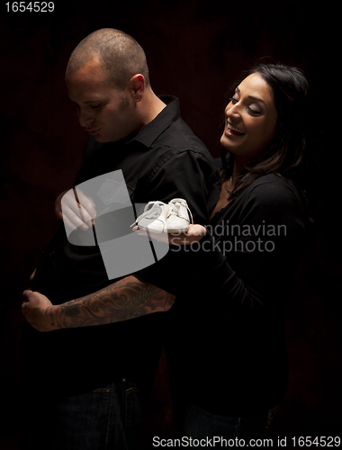 Image of Mixed Race Couple Holding New White Baby Shoes on Black