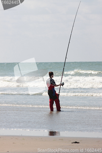 Image of fisherman casting until the fish on a sandy beach