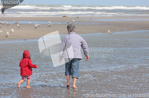 Image of Grandmother and granddaughter walking on the beach with feet in water