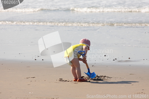 Image of young child playing with a shovel on the sand of the beach