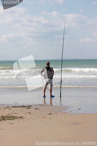 Image of fisherman casting until the fish on a sandy beach