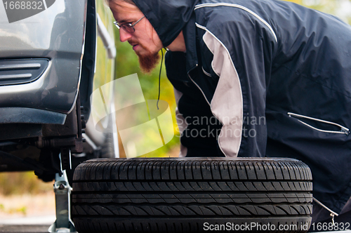 Image of Young adult inspecting the wheel of a car