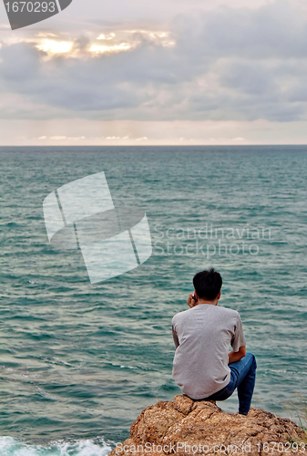 Image of A man looks into the sea while sitting on a rock 