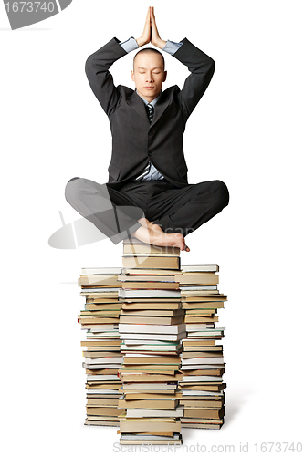 Image of businessman in lotus pose with many books near