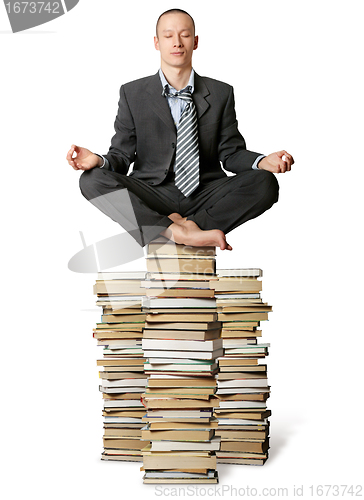 Image of businessman in lotus pose with many books near