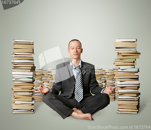 Image of businessman in lotus pose with many books near