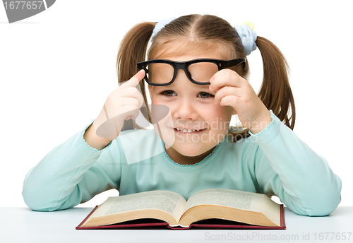 Image of Cute little girl reads a book wearing glasses