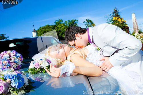 Image of groom and bride kissing on a car cowl