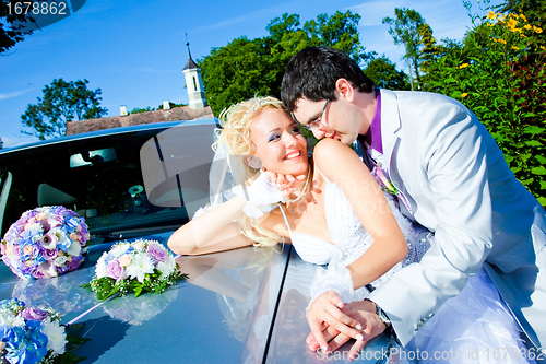 Image of groom and bride kissing on a car cowl