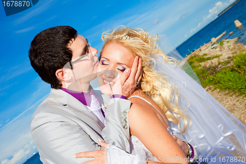 Image of tender kiss of happy groom and bride on a sea coast