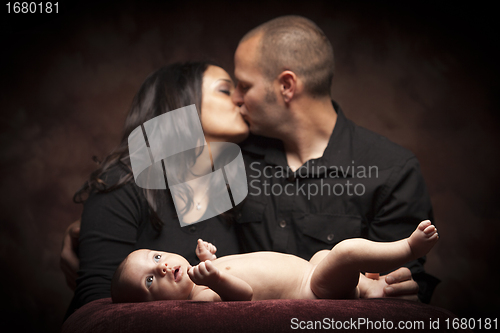 Image of Mixed Race Couple Kiss While Baby Lays on Pillow