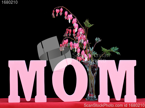 Image of The word MOM isolated on black with a vase of bleeding hearts.