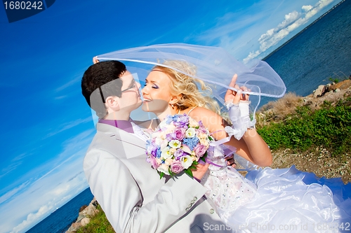 Image of tender kiss of happy groom and bride on a sea coast