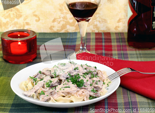 Image of Beef Stroganoff and egg noodles with wine and a lit candle.