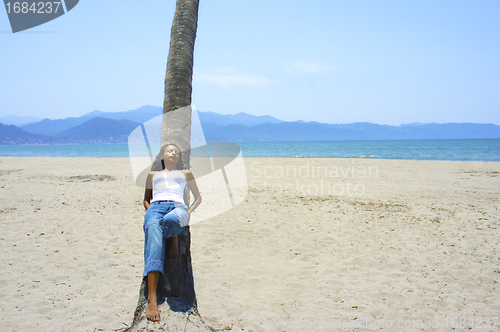 Image of Young woman leaning on a palm tree