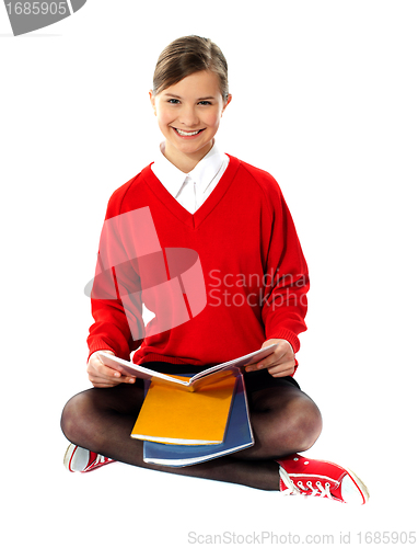 Image of Pretty school girl seated on floor, holding book