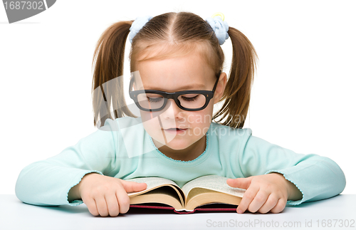 Image of Cute little girl reads a book wearing glasses