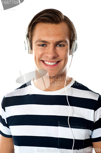 Image of Smiling young man listening to music through headphones