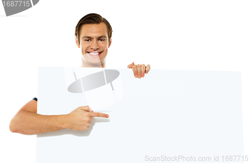 Image of Young handsome man pointing towards blank placard