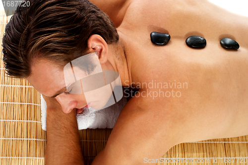 Image of Man relaxing on massage bed with hot stones