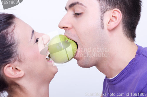Image of young couple with a green apple between their lips