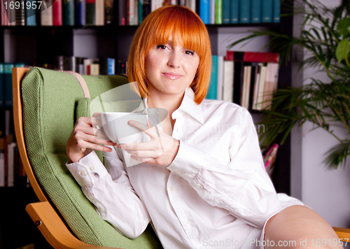 Image of woman with red hair ist sitting on a chair and drinking coffee