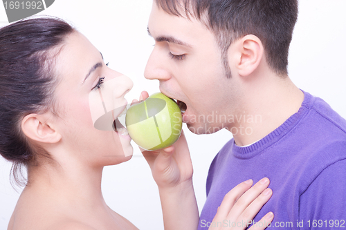 Image of young couple with a green apple between their lips