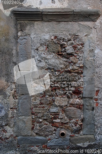 Image of Old window in gray stone wall blocked by bricks and stones