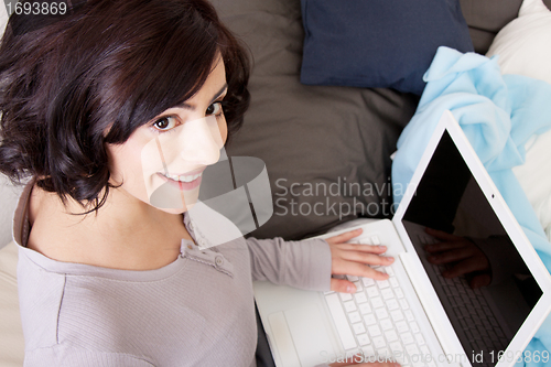 Image of young beautiful brunette woman is sitting on a sofa with a notebook