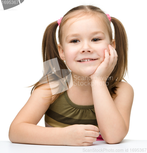Image of Happy little girl is sitting at a table and smile