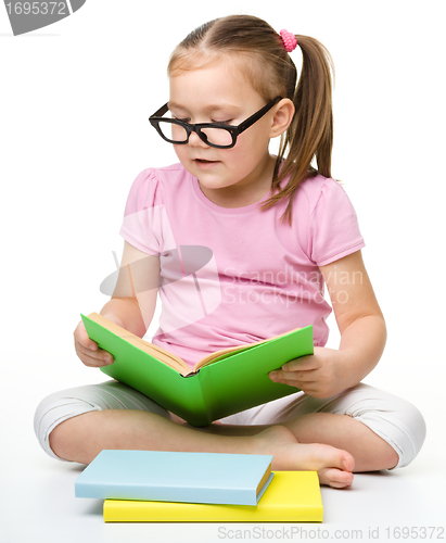 Image of Cute little girl reads a book wearing glasses