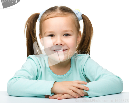 Image of Happy little girl sits at a table and smile