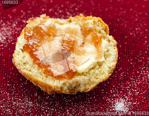 Image of Half scone with butter and jam on red tablecloth