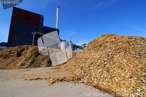 Image of bio power plant with storage of wooden fuel against blue sky