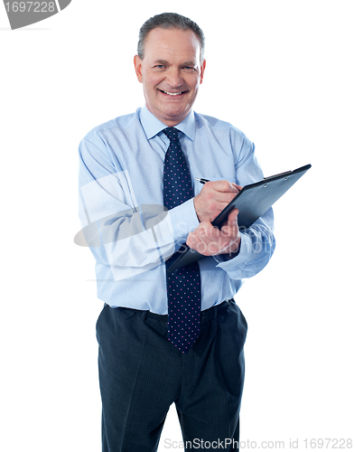 Image of A smiling ethnic businessman writing on a clipboard folder