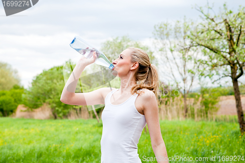 Image of young jogger is drinking water outdoor