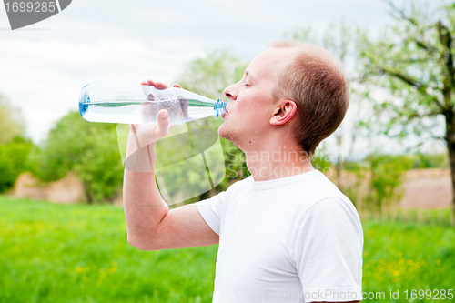 Image of young jogger is drinking water outdoor