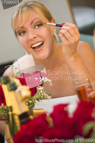 Image of Blonde Woman Applies Makeup at Mirror Near Champagne and Roses